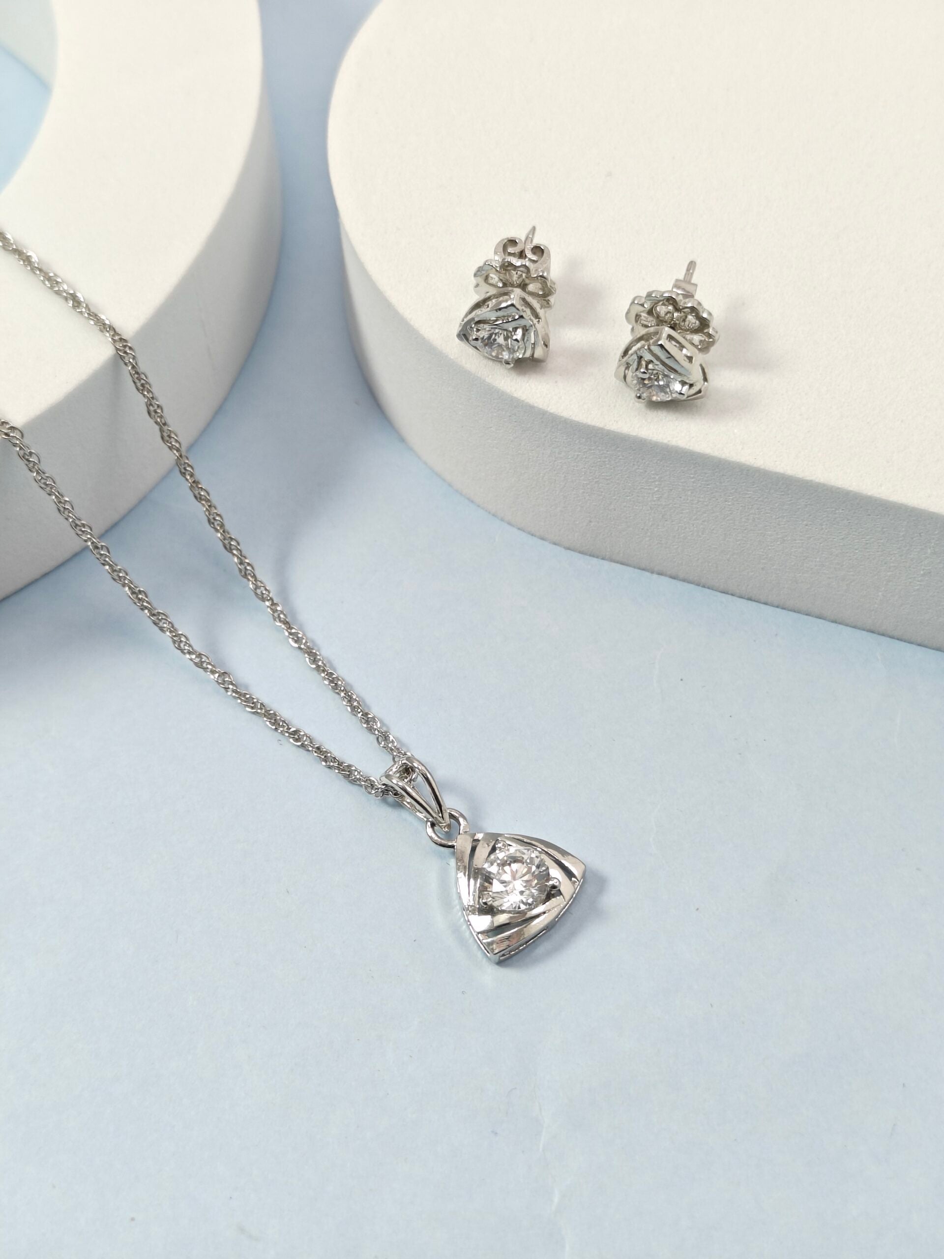 Silver necklace with heart-shaped pendant and matching earrings on a light blue background